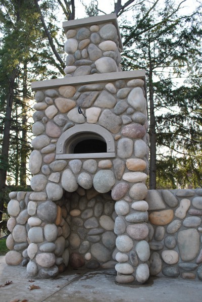 photo of a wood-fired pizza oven, built into a stone chimney on a patio outside